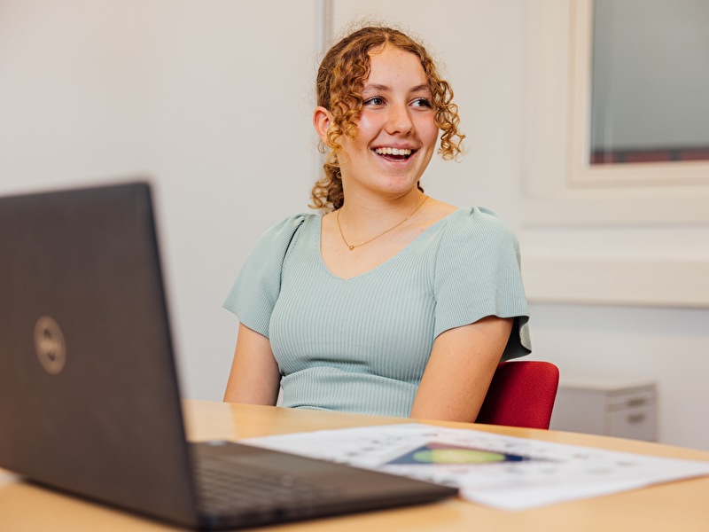 Meisje met krullende haren in een staart en een blauw shirt lacht naar de jeugdverpleegkundige